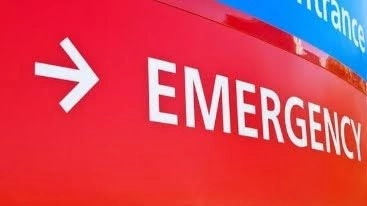 Red emergency sign with a white arrow and bold "EMERGENCY" text directs attention. Background shows part of a blue sign with "Entrance." Urgent tone.